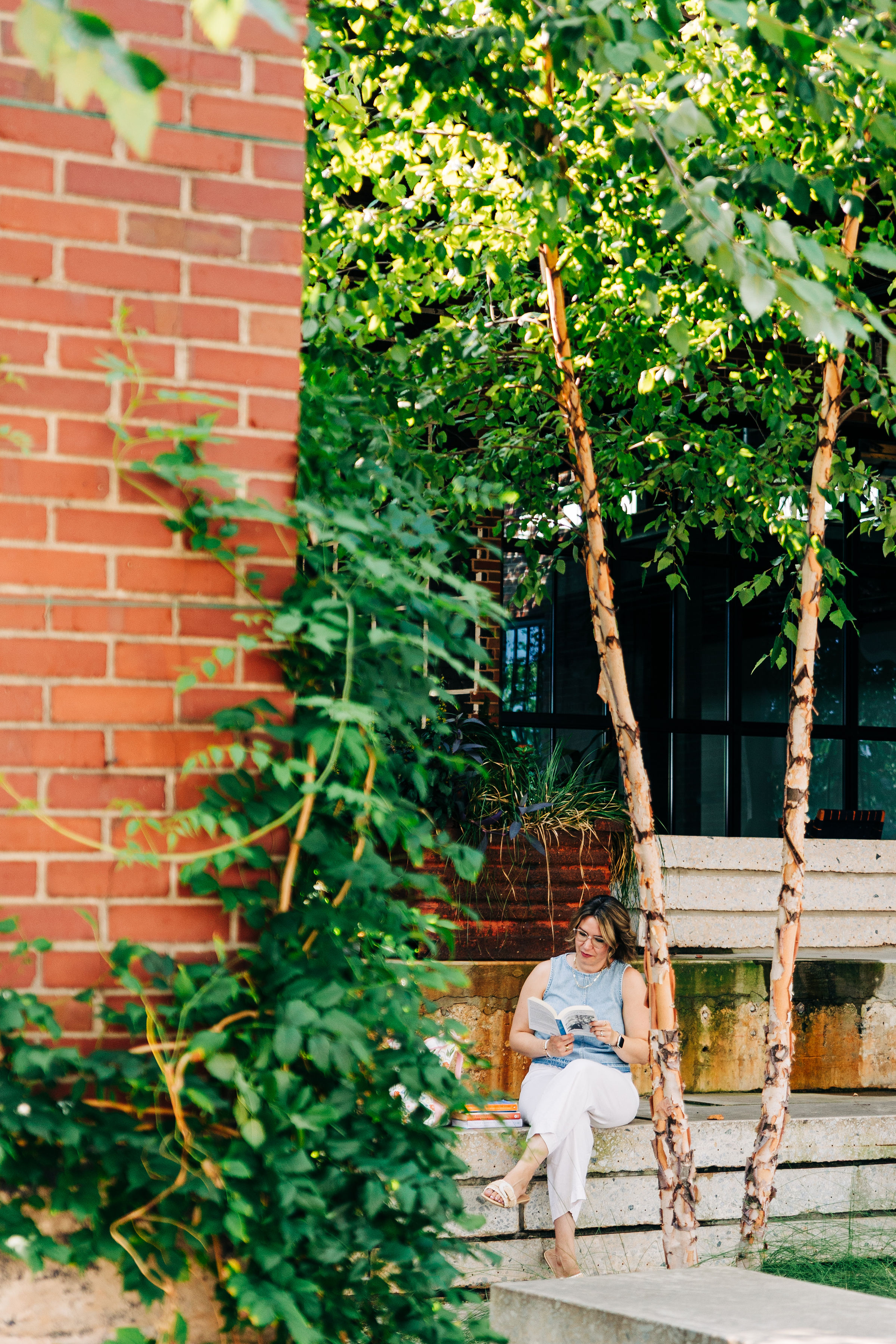 Jessie Condon sitting on stone steps under the trees, reading